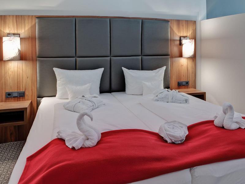 Modern hotel room with two beds, red blankets, and decorative towels shaped like animals.