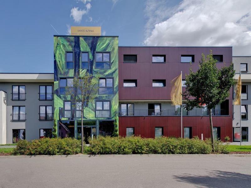 Modern two-story hotel building with colorful glass elevator and trees in front.