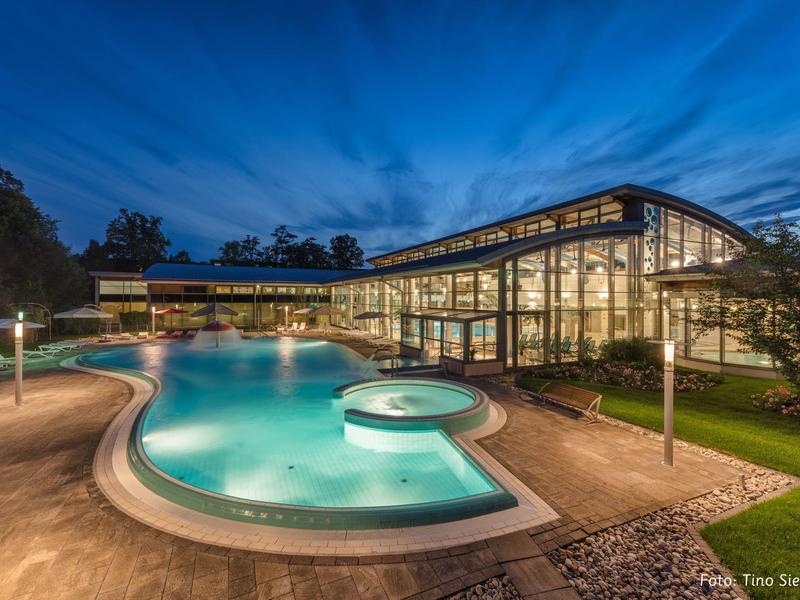 Modern hotel with large illuminated pool and glass facade at dusk