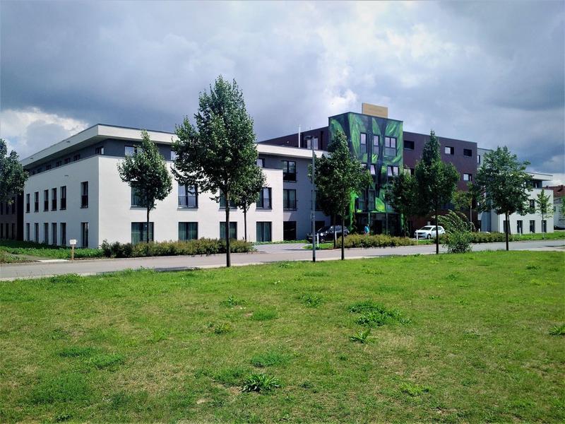 Modern hotel building with large green lawn in front under cloudy sky.