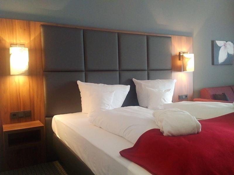 Modern hotel room with two single beds, gray headboard, and red bedspreads.
