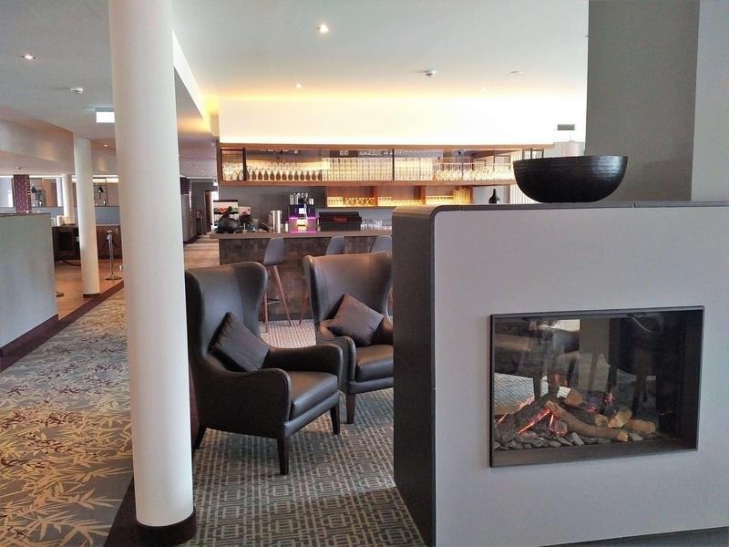 Modern hotel lounge area with fireplace, seating, and bookshelves in the background.