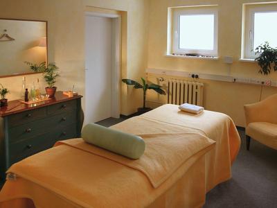 Gemütlicher Behandlungsraum mit Massageliege, grünem Sideboard, Pflanzen und warmem Licht.