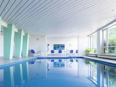 Moderner Innenpool mit blauer Wasserfläche, großen Fenstern und hellen Wänden im Schwimmbadbereich.