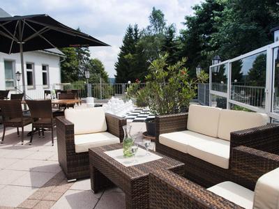 Terrasse mit braunen Sitzmöbeln aus Korbgeflecht und weißen Polstern bei bewölktem Himmel.