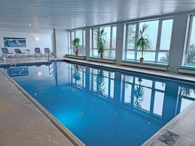 Innenpool mit blauer Wasseroberfläche und großen Fenstern mit Pflanzen davor