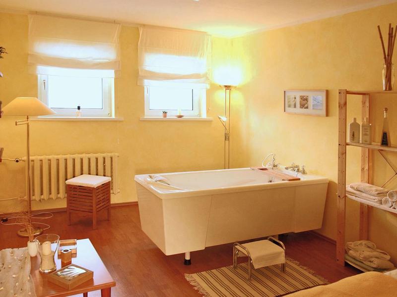 Gemütliches Badezimmer mit Wanne, Holzmöbeln, warmem Licht und zwei kleinen Fenstern.