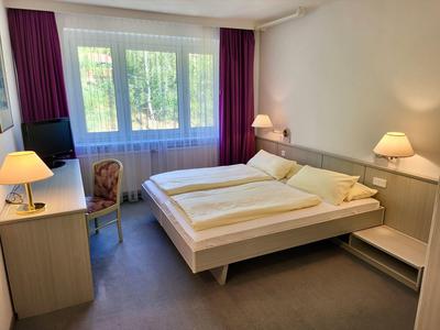 Ein einfach eingerichtetes Schlafzimmer mit Doppelbett, zwei Nachttischlampen und einem Fenster mit lila Vorhängen.