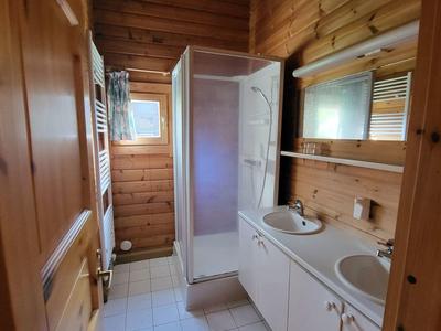 Kleines Bad mit Holzwänden, Dusche, Doppelwaschbecken und weißer Fliesenboden.