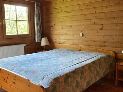 Kleines Schlafzimmer mit Holzvertäfelung, großem Bett, zwei Nachttischen und Fenster mit Vorhängen.