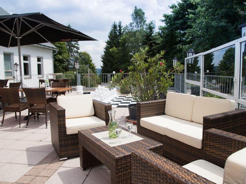 Terrassenmöbel aus braunem Rattan mit cremefarbenen Polstern auf heller Steinfläche im Außenbereich.