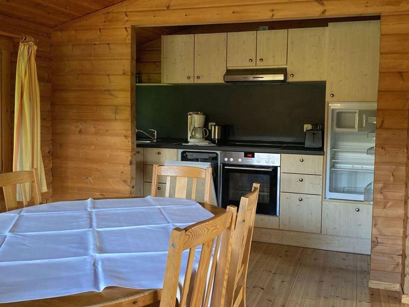 Holzraum mit Küchenzeile, Esstisch mit blauem Tuch, vier Holzstühle und großem Fenster.