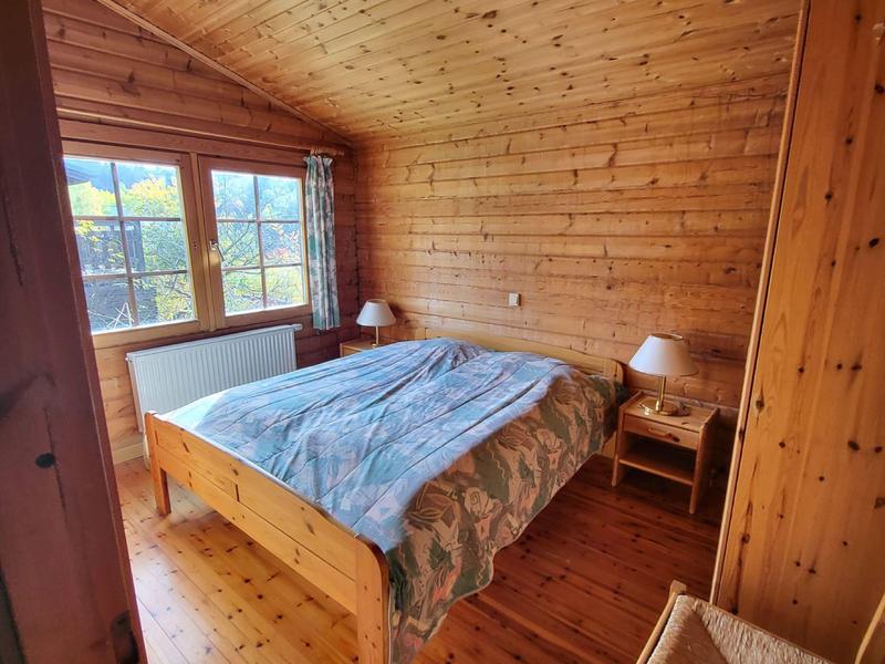 Gemütliches Schlafzimmer mit Holzwänden und großen Fenstern, Doppelbett und Nachttischen.