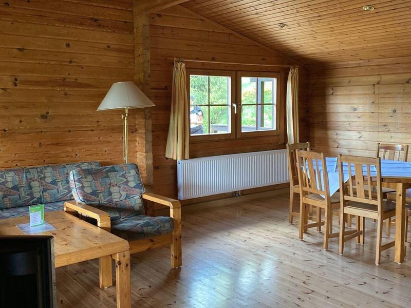 Gemütlicher Holzzimmer mit Sofa, Stehlampe, Holztisch und Essbereich mit Stühlen und Fenster.