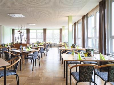 Helles, modernes Restaurant mit Holzboden, großen Fenstern und gedeckten Tischen in einem Hotel.