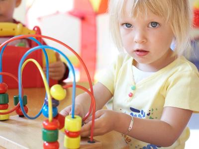 Kleines blondes Mädchen spielt konzentriert mit buntem Holzperlen-Labyrinthspielzeug.