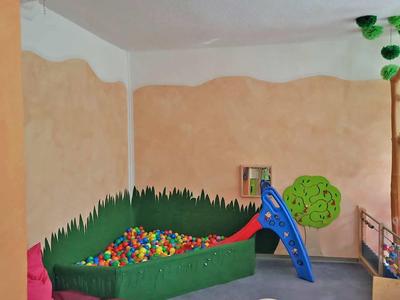 Innenraum mit Bällebad, blauer Rutsche, Wandbemalung und buntem Spielzeug für Kinder.
