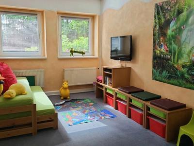 Kleines Zimmer mit grünem Sofa, buntem Teppich, Wandbild und mehrfarbigen Aufbewahrungsboxen.