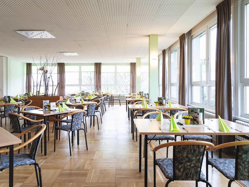 Helles, großes Restaurant mit vielen Tischen und Stühlen, großen Fenstern und Holzparkettboden.