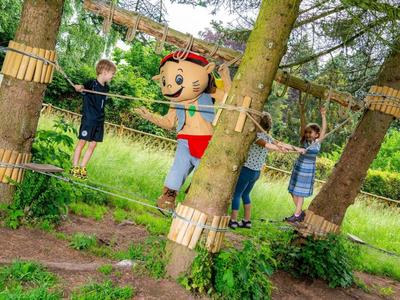 Des enfants grimpent sur un parcours de corde en plein air avec une personne en costume de mascotte coloré.