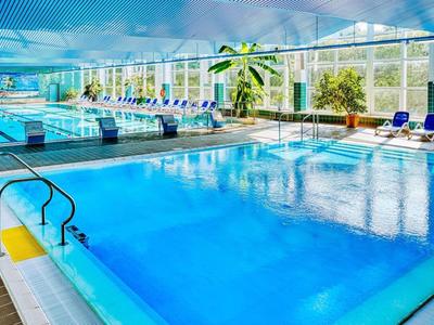 Piscine intérieure avec eau bleue claire, chaises longues et grandes fenêtres dans un hôtel.