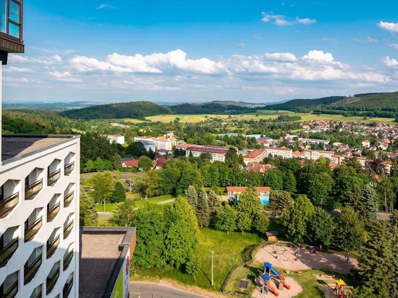 Vue d'un hôtel sur une ville avec des collines et des paysages verts sous un ciel clair.