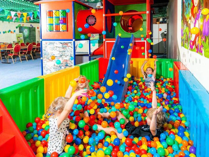 Des enfants jouent dans une piscine à balles colorée avec toboggan à l'intérieur.