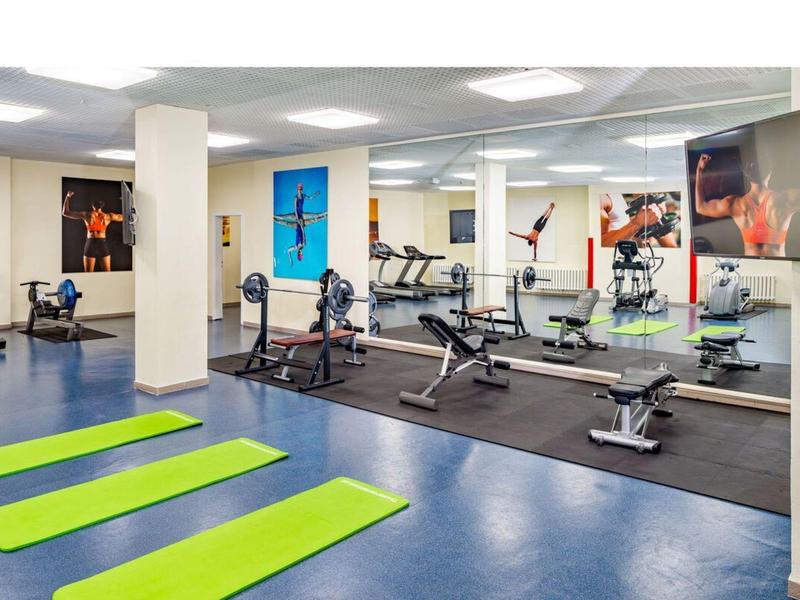 Salle de sport lumineuse avec tapis de sol, appareils de musculation et miroirs muraux.