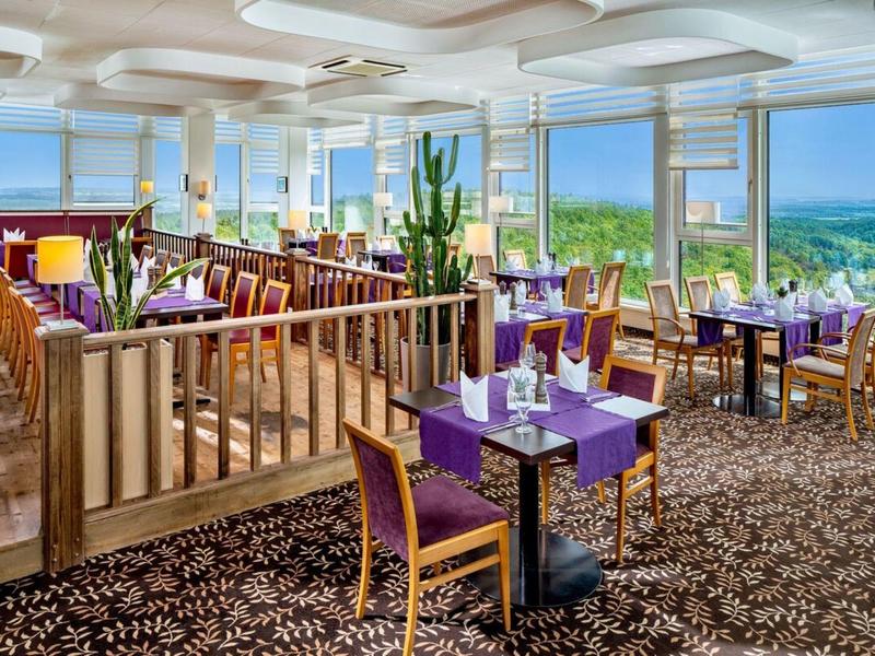 Restaurant lumineux avec des chaises violettes et des fenêtres panoramiques donnant sur la côte.