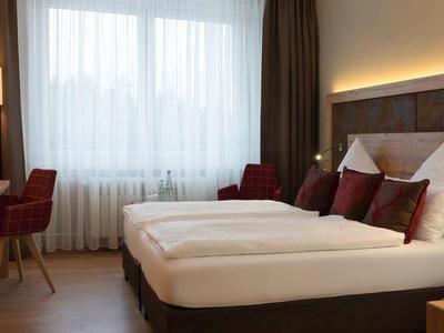 Modern hotel room with large bed, seating area, and window with daylight.