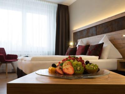 Bright hotel room with double bed, dark headboard, and fruit plate on wooden table.