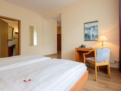 Bright hotel room with two beds, desk, chair, and bathroom in the background.