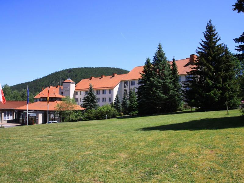 A large hotel building with red roofs, surrounded by pine trees and a large green lawn