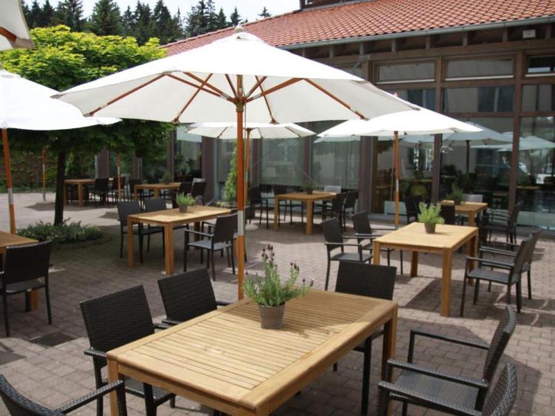 Outdoor hotel seating area with wooden tables, chairs, and white umbrellas on a paved surface.
