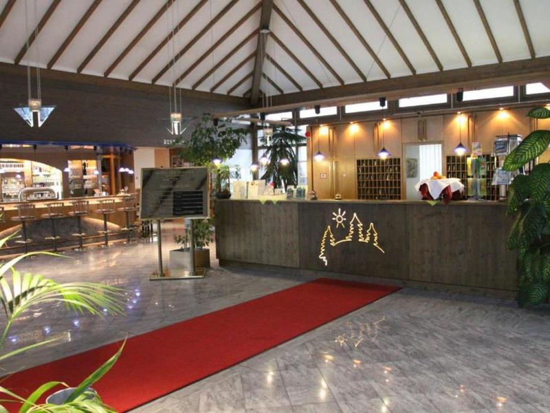 Hotel reception with desk, red carpet, and plants in a large open space.