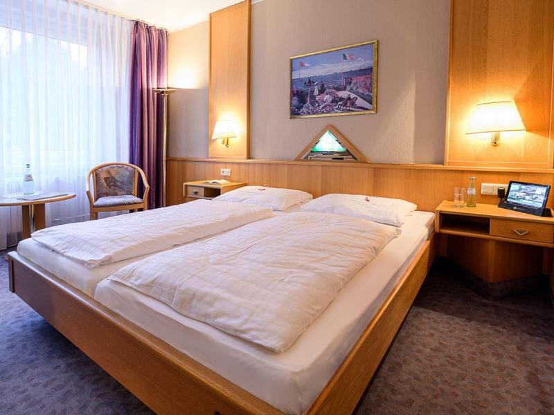 Cozy hotel room with double bed, nightstands, chair, and large window with curtains.