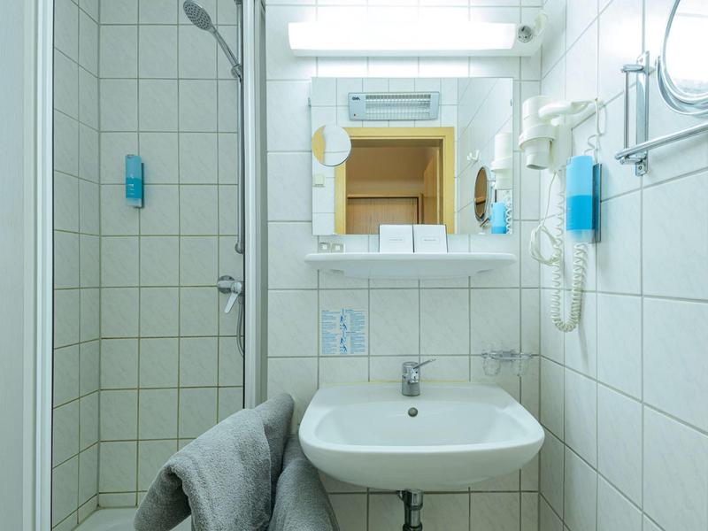 Small bathroom with white tiled walls, sink, mirror, and towel rack with towel.