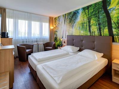 Modernes Hotelzimmer mit zwei Einzelbetten, Waldwandbild und Sitzbereich am Fenster.