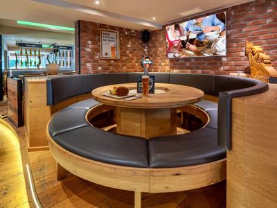 Runder Holztisch mit schwarzer Polsterung in modernem Restaurant mit Fernseher und Dekorationen.