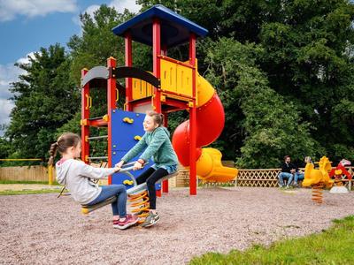 Kinder spielen auf einem bunten Spielplatz mit Rutsche und Schaukeln im Freien.