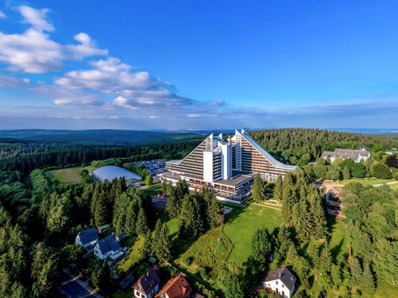Modernes Hotel mit pyramidenförmiger Architektur inmitten grüner Landschaft und Wald