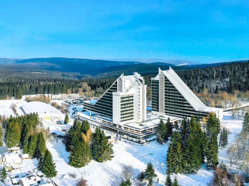 Großes Hotel mit moderner Architektur umgeben von schneebedecktem Wald und Bergen.