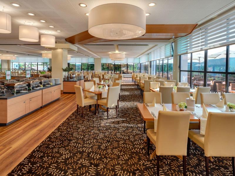 Helles Restaurant mit Holzboden, Teppich und gedeckten Tischen mit Stühlen und großer Deckenlampe.