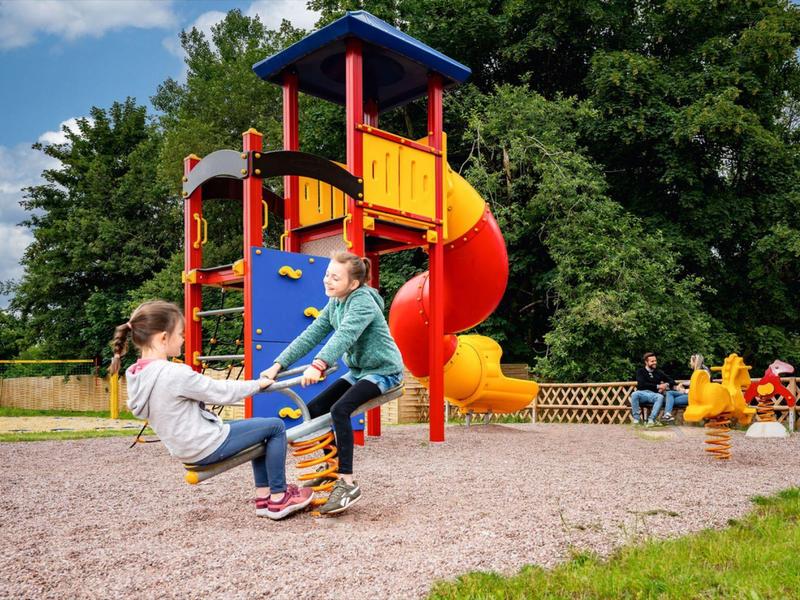 Kinder spielen auf einem bunten Spielplatz mit Rutsche und Schaukeln im Freien.