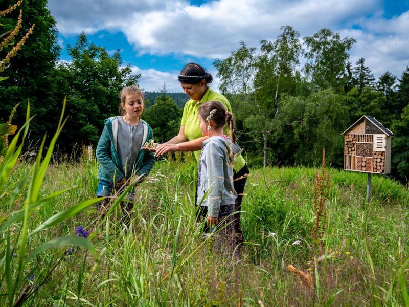 Zwei Kinder und ein Polizist in ländlicher Umgebung bei sonnigem Wetter.