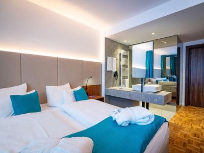 Modernes Hotelzimmer mit zwei Betten, blauen Akzenten und einem großen Spiegel über dem Waschbecken.