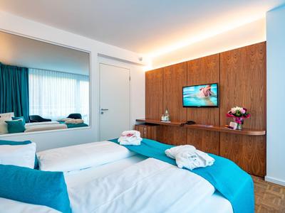 Modernes Hotelzimmer mit zwei Einzelbetten, blauen Akzenten und einem Fernseher an der Holzwand.
