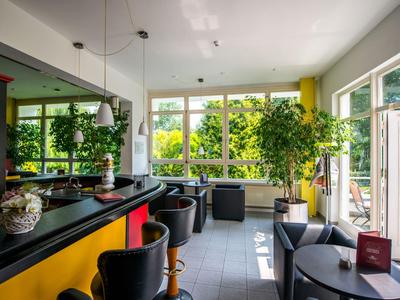 Moderner Hotelbarbereich mit gelben und schwarzen Akzenten, Sitzbereichen und großen Fenstern mit Gartenblick.