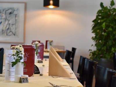 Ein gedeckter Tisch in einem Restaurant mit Menüs, blühenden Pflanzen und Stühlen im Hintergrund.