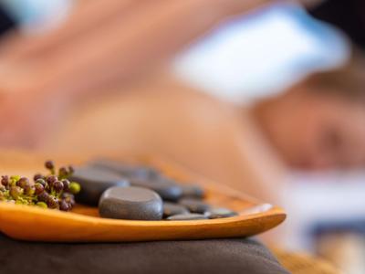 Schwarze Massage-Steine und getrocknete Blüten auf einem Tablett mit verschwommenem Hintergrund einer entspannenden Massage.